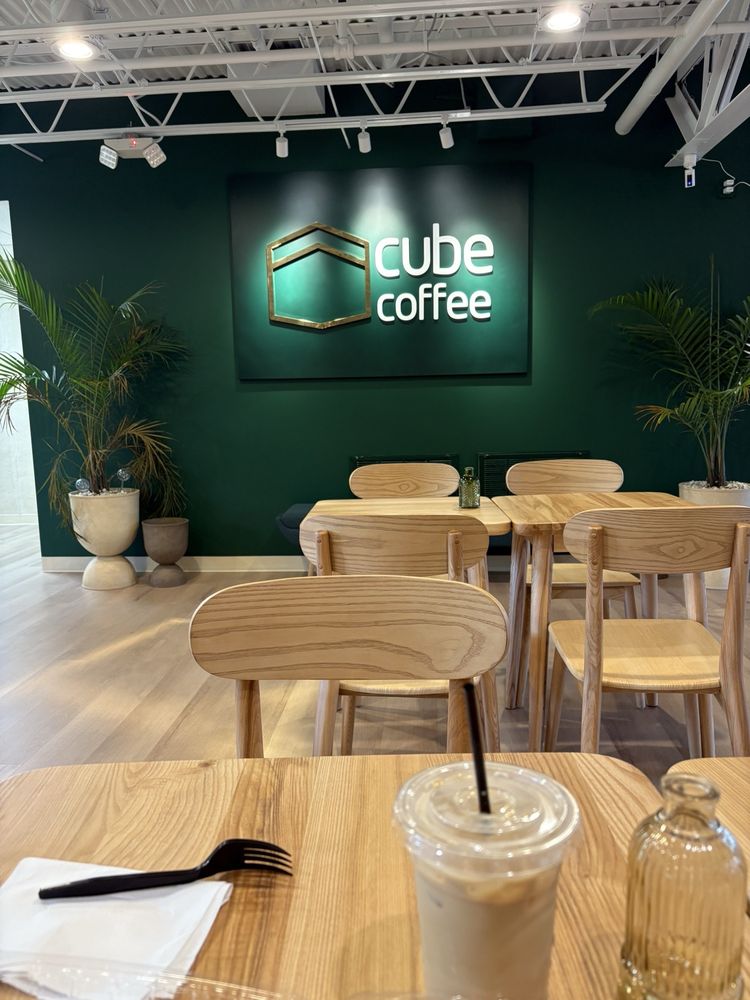 Wood tables beneath the glowing cube coffee brand wall inside the Ellicott City café