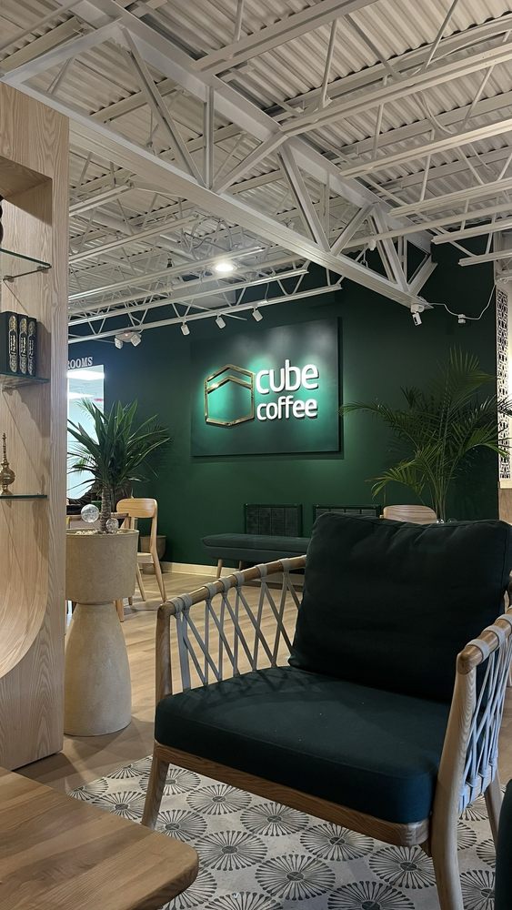 The lounge corner at Cube Coffee — deep green armchair under the glowing cube coffee logo wall